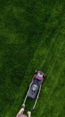 Aerial top view of man mowing grass on football stadium or lawn. Unknown man gardener cuts the grass. Garden care concept