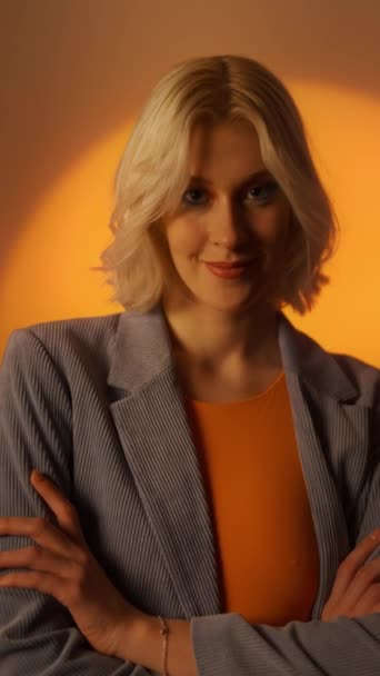オレンジ色のスタジオの背景の上にポーズジャケットの肖像若いエレガントな女性の垂直ビデオ ファッションスタジオのショットコンセプト 肖像画 — ストック動画