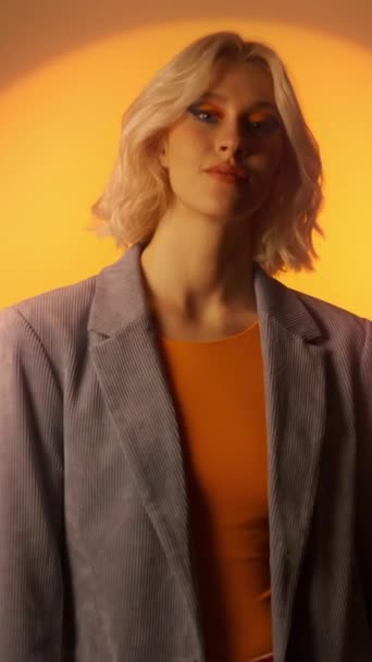年轻的女士 金发碧眼 对着相机微笑 双臂交叉地站着 在橙色墙壁上摆出一副休闲装束的漂亮模特 — 图库视频影像