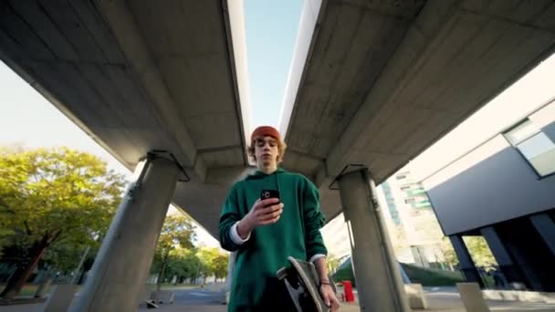 Przystojny Student Patrzący Telefon Komórkowy Spacerujący Przy Zbliżeniu Miasta Skater — Wideo stockowe