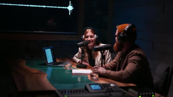 スタジオで話しているヘッドフォンを着たポジティブなカップルのラジオホスト ラジオスタジオで女性にインタビューする若い男 — ストック動画