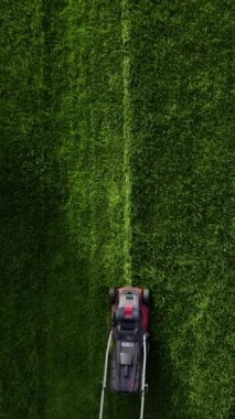Professional worker with lawn mower mows the grass, top view. Unknown man in work uniform cuts grass alone. Lawn care service concept