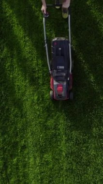 Top view of the lawn mower mows fresh, green grass on the lawn. Municipal worker in uniform with a lawn mower in his hand. Lawn care service concept