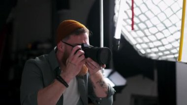 Fotoğraf stüdyosunda fotoğraf çekerken kamerayı kullanan sakallı genç fotoğrafçı. Mesleki meslek kavramı