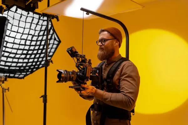 A person is using a camera in front of a yellow backdrop while capturing video at an event. The camera accessory is essential for recording fun music and audio equipment