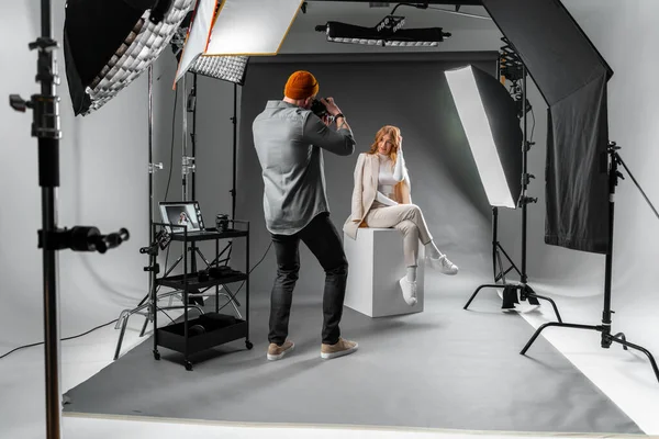 Bir adam, bir fotoğraf stüdyosundaki küpte poz veren bir kadını profesyonel fotoğraf ekipmanları ve stüdyo eşyaları ile bir etkinliği kutlarken yakalıyor.