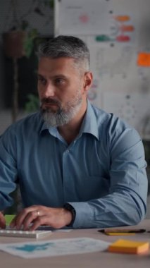 Modern ofis alanında çalışmak için bilgisayar kullanan şık günlük gömlekler giyen odaklanmış beyaz bir adam. Olgun ofis çalışanı e- postaları cevaplıyor, klavyeyi daktilo ediyor