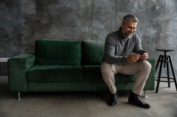 Mann Sitter Komfortabelt Grønn Sofa Bena Krysset Mens Han Mobiltelefonen – stockfoto