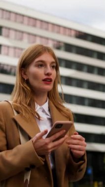 Kendine güvenen genç bir bayanın akıllı telefonuyla şehir caddesinde tek başına yürüdüğü dikey bir manzara. Başarılı bir iş kadını. Görüşmek için acele ediyor. Arayıp duruyor.