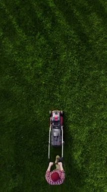 Top view of the lawn mower mows fresh, green grass on the lawn. Municipal worker in uniform with a lawn mower in his hand. Lawn care service concept