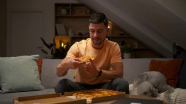 Evde köpekle pizza yiyen genç bir adam. Aile bireyleri olarak hayvan kavramı