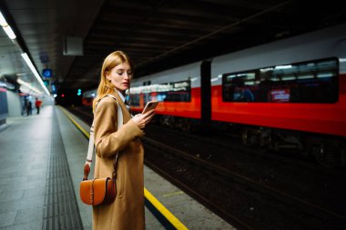 Takım elbiseli ciddi bir iş kadını metroda akıllı telefondan kablosuz internet geziyor. Kadın metro istasyonunda cep telefonuyla duruyor, sosyal medya kullanıyor ve tren bekliyor.