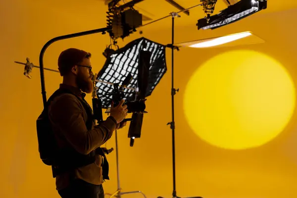 映画スタジオでカメラで大きな黄色の背景をキャプチャする男 明るい背景にシルエットを作成する ストックフォト