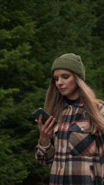 Portrait of young hiker woman using mobile phone navigation or social media app. Girl walking down the road and looks at her phone