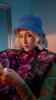 Moda modası geçmiş bir kadın, akşam stüdyo arka planında koltukta oturuyor ve internette akıllı telefonlarda geziniyor.
