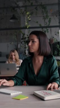 Modern çalışma ofisinde çalışmak için bilgisayar kullanan şık tişörtler giyen odaklanmış beyaz bir kadın. Esmer ofis çalışanı e- postaları cevaplıyor, açık alanda klavye yazıyor
