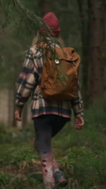 Back view of the woman in autumn clothes walking in autumn forest. Female hiker with backpack going up through wet wood with green trees
