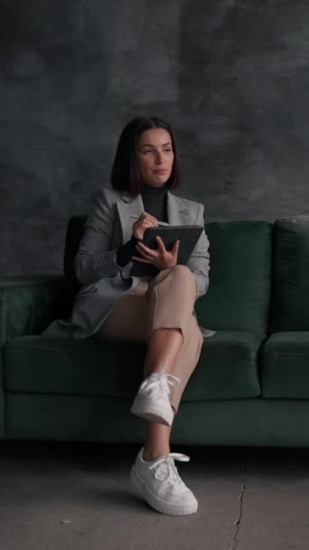 若い女性デザイナーは ロフトリビングルームの緑のソファに座ってタブレットコンピュータに描画します 一人で建築プロジェクトを準備する創造的な女性 — ストック動画