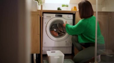Genç esmer kadın çamaşır makinesine çamaşır koyuyor ve evde çamaşır yıkarken onu açıyor. Ev içi rutin kavram