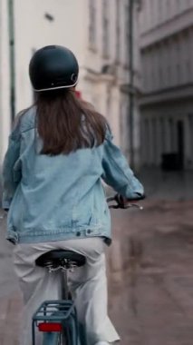 Şehir merkezinde yağmurlu cadde boyunca bisiklet süren güzel genç bir kadının arka manzarası. Etkin yaşam tarzı kavramı