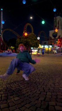 Lunaparktaki sokakta müzik dinleyen ve dans eden genç beyaz adamın dikey görüntüsü.