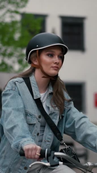 ヨーロッパの都市の通りで自転車に乗っているヘルメットの深刻な少女のゆっくりとした動きのビュー 夏の旅行手段で自転車を使用して笑顔の若い女性ライフスタイル Ecoフレンドリー ストック映像