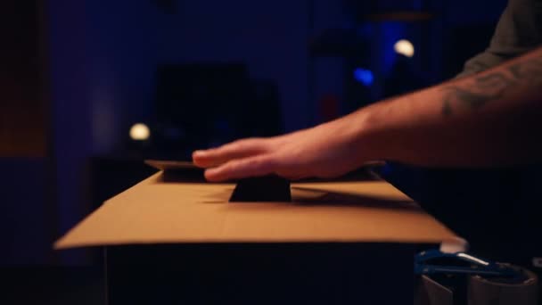 タトゥーされた男の手の包装の食器棚箱および夕方の部屋に粘着テープを置くことの閉鎖 パッキング小包の概念 ロイヤリティフリーのストック動画