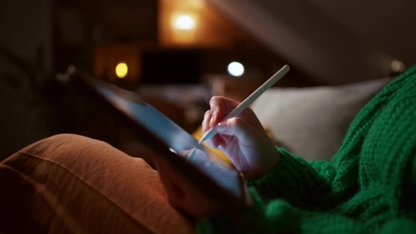 若い女性は 夕方に居心地の良いスタイリッシュな家に座って デジタルタブレットに描いた 気軽に創造的な仕事を持っている服を着た ストック動画