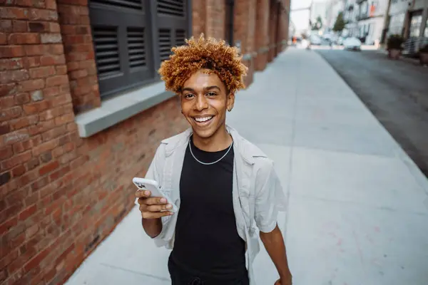 Молодий Чоловік Футболці Верхньому Одязі Посміхається Ходячи Тротуару Тримаючи Мобільний Ліцензійні Стокові Фото