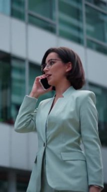 Cute businesswoman having conversation on smartphone outdoors. Portrait of beautiful caucasian female business person who talking on cell phone dressed green suit standing city street