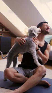 Bir adam yoga minderinde oturuyor, rahatça elinde bir köpek tutuyor. Köpeğin bıyıkları vardır ve uyluğunda dinlenirken, adam parmaklarıyla hareket eder.