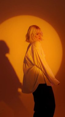 Blonde-haired joyful girl in white shirt dancing with inspired face expression. Active young woman in casual summer outfit having fun indoor