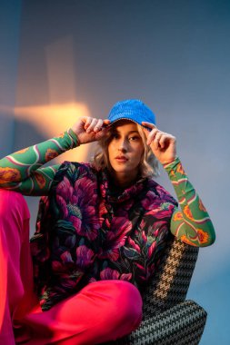 Bir kadın eğlenceli bir mavi şapka takıyor. Flaş fotoğrafçılık, giydiği canlı mor şapkayı yakalıyor ve sahne sanatları sahnesine eğlence katıyor.