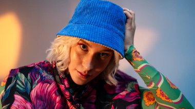 Havalı hippi öğrenci kadın şık giyinmiş kameraya bakıyor ve şapkasını düzeltiyor. Beyaz kadın model koltukta oturuyor.