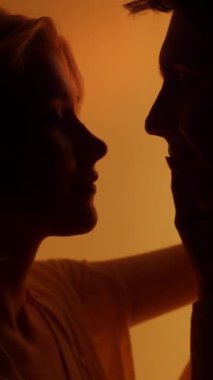 Romantik bir randevu sırasında, parlak turuncu neon ışığı altında öpüşen genç bir çift. Duygular konsepti