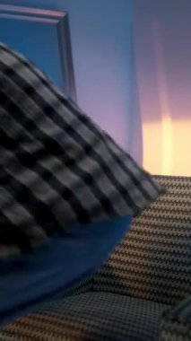 Handsome trendy young model posing at the evening studio background, sitting in a armchair and browsing on his mobile phone