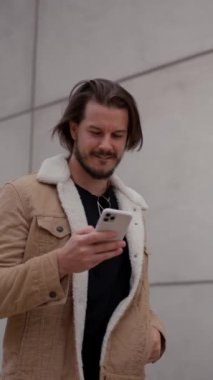 Genç adam şehirde yürürken akıllı telefon kullanırken mutlu bir şekilde gülümsüyor. Boş caddede tek başına dolaşırken hafta sonunun tadını çıkarmakla meşgul bir işadamı.
