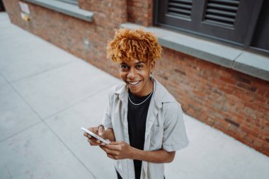 Genç adam kaldırımda elinde bir cep telefonuyla dikiliyor. Başparmağı ekranda süzülüyor. Binaların ön cephesindeki tuğla işçiliğine hayran..