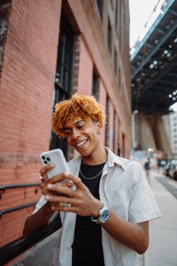 Kaldırımda cep telefonu kamerasıyla gülümseyen genç adam.