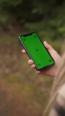 Cropped view of the hiker woman using chromakey mobile phone navigation or social media app. Girl walking down the road and looks at her phone with green screen