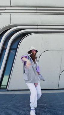 Fashion cutte woman with sunglasses and hat dancing outside looking at camera. Female dancer performing dance show making freestyle stunts. Funny stylish caucasian hip hopgirl. High quality 4k footage