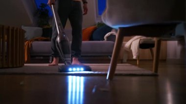 Akşam evde elektrikli süpürge kullanan genç adam, yakın plan. Geceleri evi temizleyen tanınmayan bir adam. 
