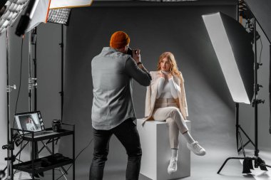 Bir adam, bir fotoğraf stüdyosundaki küpte poz veren bir kadını profesyonel fotoğraf ekipmanları ve stüdyo eşyaları ile bir etkinliği kutlarken yakalıyor.
