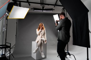 Bir adam, bir fotoğraf stüdyosundaki küpte poz veren bir kadını profesyonel fotoğraf ekipmanları ve stüdyo eşyaları ile bir etkinliği kutlarken yakalıyor.