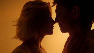 Sevgililer Günü 'nde canlı turuncu ışıklı stüdyo arka planında öpüşen ve birbirine dokunan genç çift.