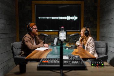 Yayın stüdyosunda mikrofonların yanında oturmuş gülümseyen iki radyo sunucusu. Yaratıcı işgal kavramı