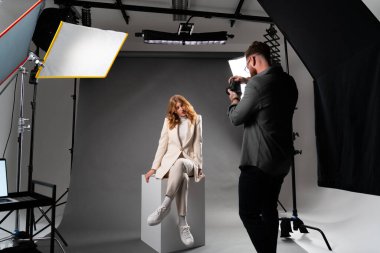 Profesyonel stüdyo ortamında beyaz küple poz veren bir model, bir fotoğrafçı tarafından fotoğraflanıyor..