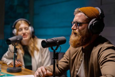 İki podcast sunucusu modern bir stüdyoda kayıt yapıyorlar, kulaklık takıyorlar, çeşitli konuları tartışıyorlar..