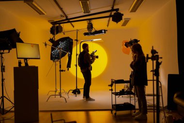 Bir kameraman, sanat ve görsel sanatlar dünyasına dalmış canlı sarı bir arkaplanı olan bir film stüdyosunda bir görüntü yakalıyor..