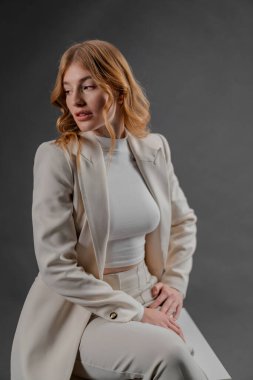 Beyaz takım elbiseli zarif bir kadın bir stüdyoya özgüven yayar. Duruş ve entelektüellik onun tarzıyla harmanlanır.